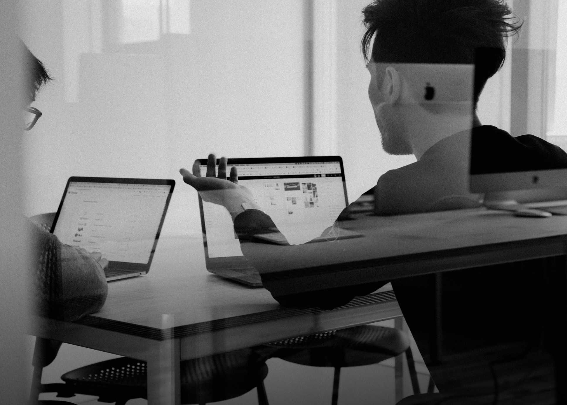Black and white image of 2 people infront of computers in a small office room